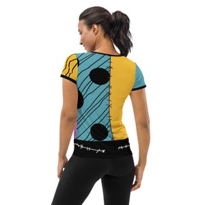 May include: A blue and yellow short-sleeved t-shirt with a patchwork design featuring black circles and stitching. The shirt has a black band at the bottom with stitching.