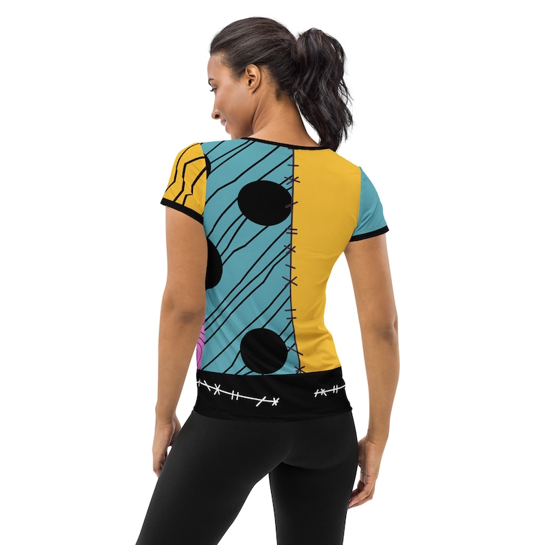 May include: A blue and yellow short-sleeved t-shirt with a patchwork design featuring black circles and stitching. The shirt has a black band at the bottom with stitching.