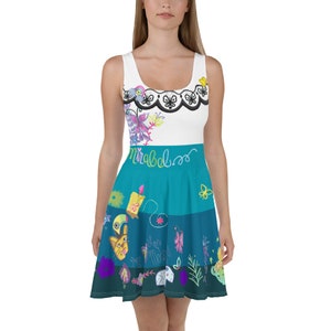 Puede incluir: Un vestido blanco y azul sin mangas con un estampado floral colorido y la palabra "Mirabel" escrita en la parte delantera. El vestido tiene un corpiño ajustado y una falda acampanada.