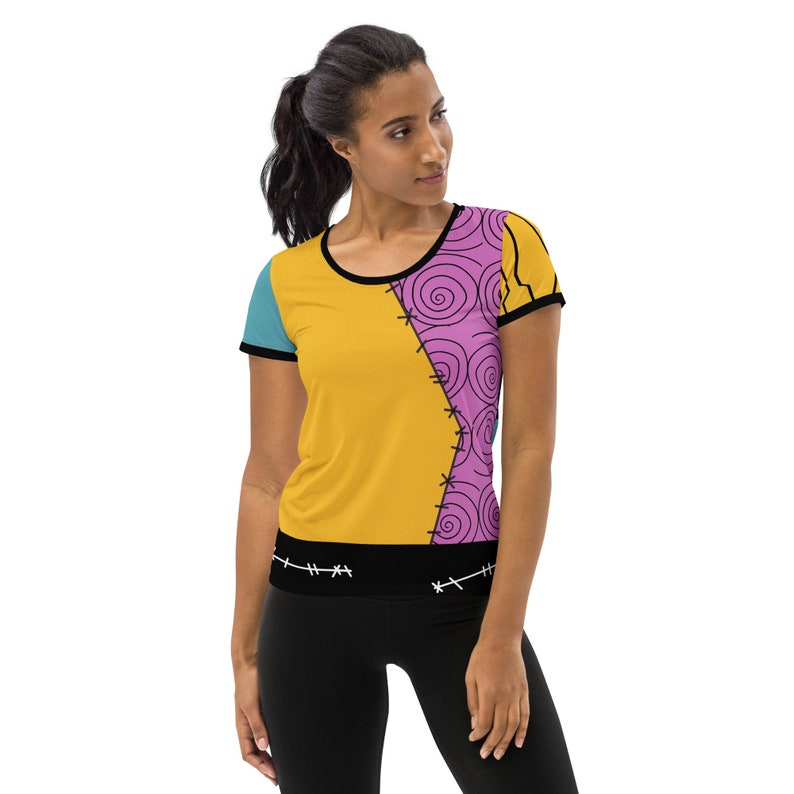 May include: A yellow, pink, and blue short-sleeved t-shirt with a stitched design. The shirt has a black band around the bottom with white stitching.