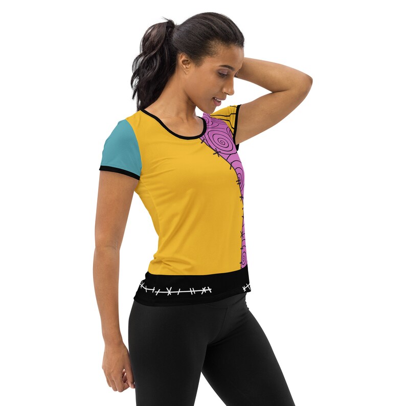 May include: A yellow, blue, and pink short-sleeved shirt with a stitched design. The shirt has a black band with white stitching around the waist.