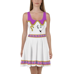 Puede incluir: Vestido skater blanco con diseño de taza de dibujos animados. El vestido sin mangas tiene un corpiño morado con ribete amarillo y una falda blanca. La cara de la taza está impresa en el corpiño, con un borde decorativo en la cintura y el dobladillo.