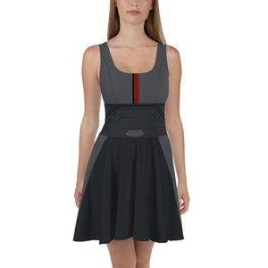 Könnte beinhalten: Ein ärmelloses graues und schwarzes Kleid mit einem roten Streifen in der Mitte. Das Kleid hat einen figurbetonten Oberteil und einen ausgestellten Rock.