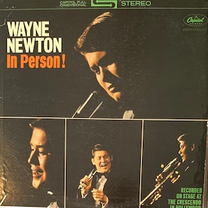 May include: A vintage vinyl record album cover featuring Wayne Newton. The cover is black with a white border and features a photo of Wayne Newton in a black suit. The album title is "Wayne Newton In Person!" and the record label is Capitol Records. The album was recorded on stage at The Crescendo in Hollywood.