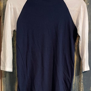 Puede incluir: Una camiseta de b&eacute;isbol azul marino y blanca con manga tres cuartos.