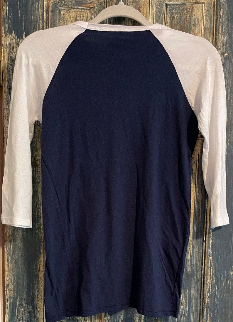 Puede incluir: Una camiseta de b&eacute;isbol azul marino y blanca con manga tres cuartos.