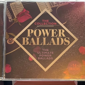 May include: A CD case with a gold diamond-shaped design featuring the text "The Collection Power Ballads The Ultimate Power Ballads" and a red rose with petals scattered around the case. The case has a black background with a blurred image of a guitar in the background. The text "14 Tracks" is in the lower right corner of the case.