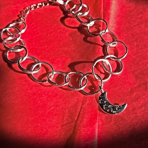 May include: A silver chain necklace with a crescent moon charm. The chain is made of interlocking circles and the moon charm has a star design.