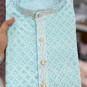 May include: A light blue kurta shirt with intricate white and gold embroidery. The shirt features a mandarin collar and decorative buttons down the front. The fabric has a geometric pattern.