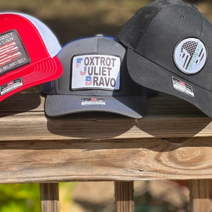May include: Three baseball caps with different designs. One is red and white with the text "WHEN TYRANNY BECOMES LAW REBELLION BECOMES DUTY". Another is gray with the text "FOXTROT JULIET BRAVO". The third is black with a white patch.