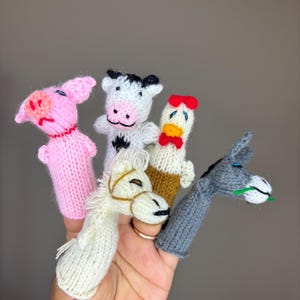 May include: Five knitted finger puppets depicting farm animals: a pink pig, a black and white cow, a brown chicken, a white horse, and a gray donkey.