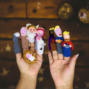 May include: A collection of handmade finger puppets depicting nativity characters. The puppets are made of knitted yarn in various colors, including white, brown, blue, and pink. The set includes figures of the baby Jesus, Mary, Joseph, angels, and the three wise men.