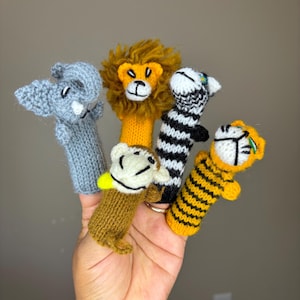 May include: Five finger puppets made of knitted fabric. The puppets are shaped like a lion, zebra, elephant, monkey, and tiger. The puppets are all wearing different colors and patterns.