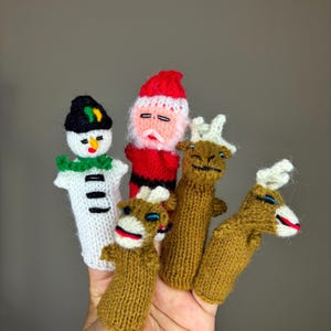 May include: Set of five knitted finger puppets featuring a snowman, Santa Claus, and three reindeer. The puppets are brown, white, red, and green.
