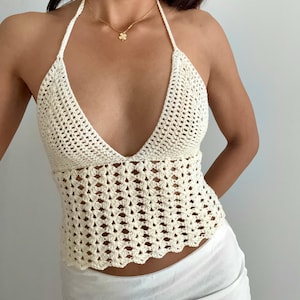 Puede incluir: Top halter de ganchillo color crema con cuello en V profundo y dobladillo festoneado. El diseño de tejido abierto crea un aspecto texturizado. Se ve un collar dorado con un colgante de trébol.