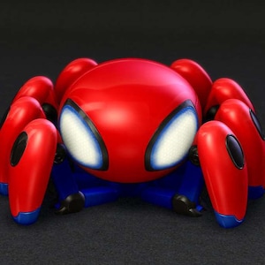 May include: A red and blue toy spider with large, white-rimmed eyes. The toy has a rounded red body and eight red legs with blue accents. The toy is a stylized representation of a spider.
