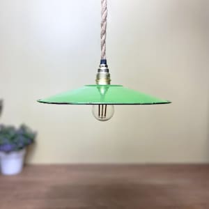 May include: A green pendant light with a circular shade and a visible lightbulb. The light hangs from a twisted rope cord. The fixture has a vintage, industrial style.