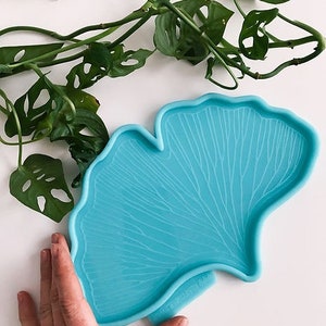 Può includere: Uno stampo in silicone blu chiaro a forma di foglia di ginkgo. Lo stampo presenta un motivo di venature dettagliato e un bordo liscio leggermente curvo.