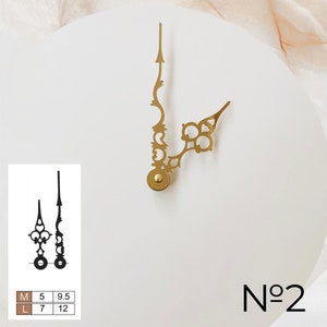 May include: Gold-colored clock hands with ornate designs, including a minute hand with an arrow-like tip and an hour hand with a decorative end. A smaller black pair of hands is shown below, with size details. The number "No 2" is printed in black.