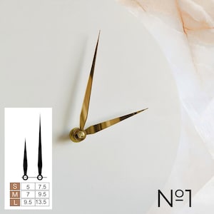 May include: Gold-colored clock hands on a white background. The hands are thin and elegant, with a classic design. A small chart shows black clock hands with measurements in inches for sizes S, M, and L. The number "N&ordm;1" is in the bottom right corner.