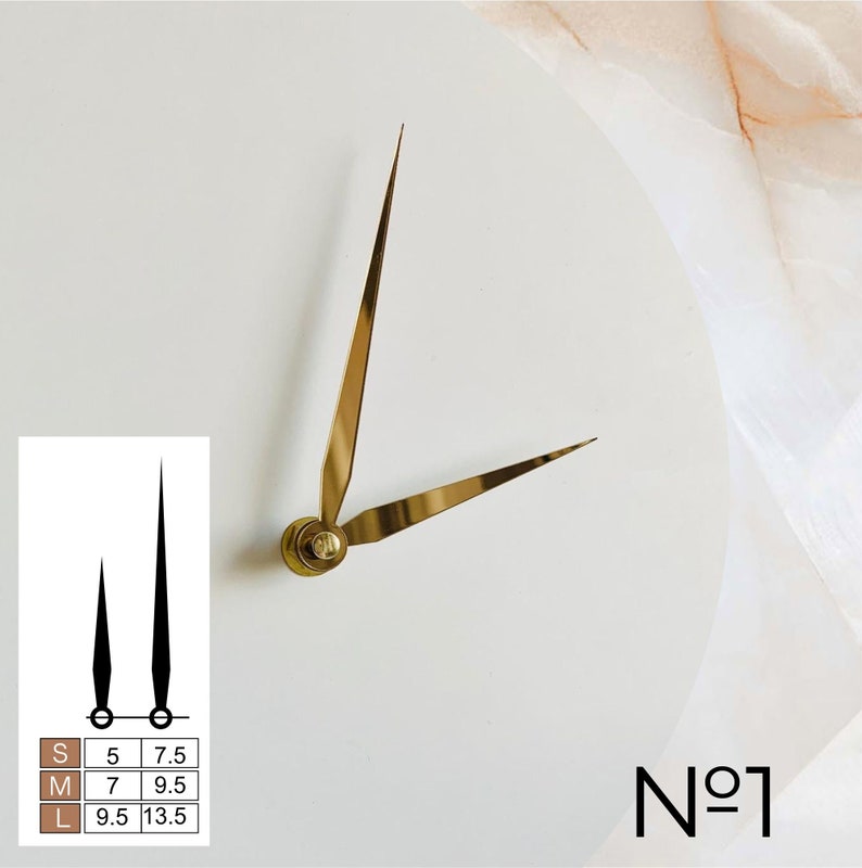 May include: Gold-colored clock hands on a white background. The hands are thin and elegant, with a classic design. A small chart shows black clock hands with measurements in inches for sizes S, M, and L. The number "N&ordm;1" is in the bottom right corner.