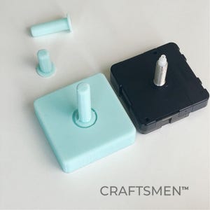 Könnte beinhalten: Ein hellblauer quadratischer Uhrwerk mit einer weißen Kunststoffspindel und ein schwarzes Uhrwerk mit einer silbernen Spindel. Die Uhrwerke befinden sich auf einer weißen Oberfläche. Der Text "CRAFTSMEN™" ist in der rechten unteren Ecke des Bildes sichtbar.