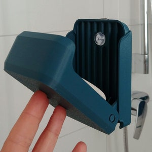 One hand closing a 3d printed blue soap box under the shower, containing solid shampoo. It hangs from a suction cup. Wall mounted