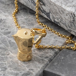 May include: A gold chain necklace with a gold-colored pendant shaped like a traditional Italian coffee pot.