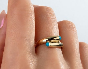 Può includere: Un anello d'oro con due pietre turchesi incastonate nella fascia. L'anello è indossato su un dito.