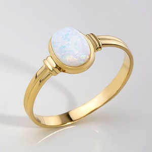 May include: A gold ring with a white oval opal gemstone. The ring has a simple design with a smooth band.