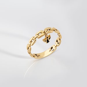 May include: A gold ring with a chain-like design and a small angel charm hanging from it.
