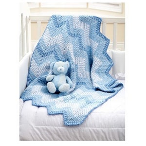 Peut inclure: Une couverture pour bébé en crochet bleu et blanc avec un bord festonné, sur laquelle est assis un ours en peluche bleu.