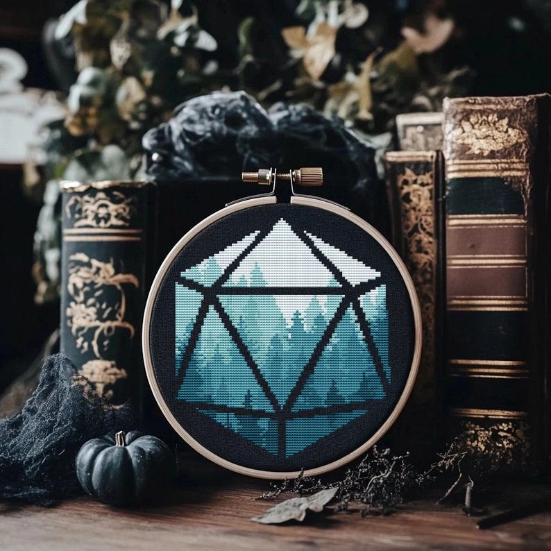 May include: A cross-stitch embroidery hoop with a blue and green forest scene inside a black and white geometric shape, resembling a twenty-sided die.