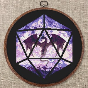 May include: A cross-stitch artwork of a dragon inside a geometric shape, mounted in a wooden embroidery hoop. The dragon is dark purple with outstretched wings, set against a background of light purple and white. The hoop is approximately 10 inches in diameter.