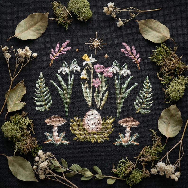 Puede incluir: Un dise&ntilde;o de punto de cruz con un arreglo floral central con flores blancas, rosas y amarillas, rodeado de follaje verde y setas. El dise&ntilde;o est&aacute; sobre un fondo negro, enmarcado con hojas secas y musgo.