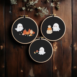 Peut inclure: Trois œuvres d'art au point de croix encadrées sur le thème d'Halloween. Chacune présente un fond noir et un cerceau en bois. Les motifs comprennent un fantôme blanc avec des citrouilles, un fantôme avec des citrouilles empilées et un fantôme avec des champignons.