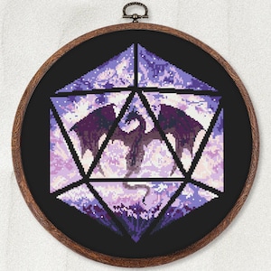 May include: A cross-stitch design of a dragon inside a D20 die, framed in a wooden hoop. The dragon is dark purple, set against a light purple and white background. The die is outlined in black.