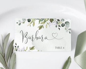 May include: A rectangular place card with the name "Barbara" in elegant black script, accented by a heart symbol. The card features watercolor-style green foliage and the text "TABLE 4".
