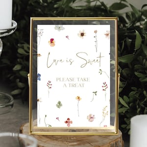 May include: A gold-framed sign with a white background and floral illustrations. The sign reads "Love is Sweet" and "Please Take a Treat".