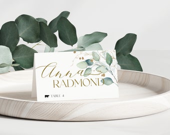 May include: White place card with gold lettering and a watercolor eucalyptus design. The name "Anna Radmond" is written in cursive. The text "Table 4" is printed below the name.
