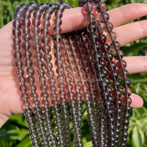 Pode incluir: Várias mechas de contas de quartzo fumê em tons de marrom e cinza. As contas são redondas e enfiadas, com uma aparência translúcida. A imagem inclui o texto "https://shoplarafinds.etsy.com."