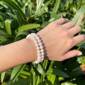 May include: A white pearl bracelet with two strands of pearls. The bracelet is worn on a person's wrist.