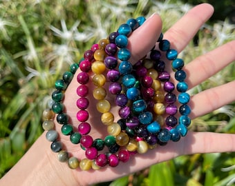 May include: A set of six colorful tiger's eye gemstone bracelets. The bracelets are stacked on top of each other and feature different shades of blue, green, gold, and red.