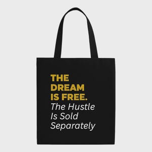 Może przedstawiać: Czarna torba typu tote z napisem "THE DREAM IS FREE. The Hustle Is Sold Separately" w kolorze złotym i białym. Torba ma dwa czarne uchwyty i jest wykonana z wytrzymałego materiału. Motywacyjny dodatek do codziennego użytku.