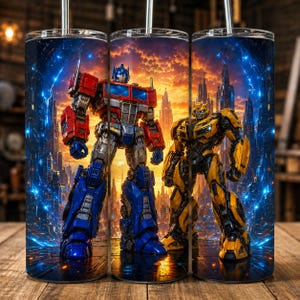 May include: A cylindrical metal tumbler featuring a full-wrap graphic of Optimus Prime in red and blue and Bumblebee in yellow standing before a futuristic city skyline at sunset with glowing blue light streaks and a metallic straw on top.