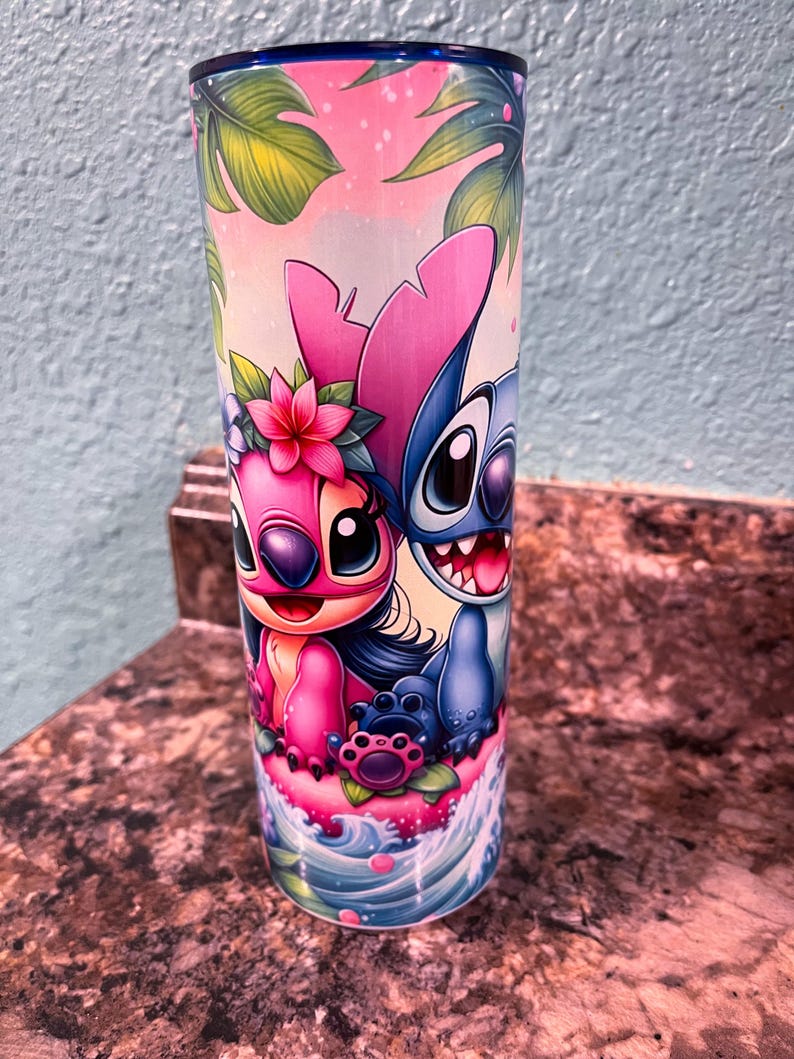 May include: A stainless steel tumbler with a colorful design featuring Stitch and Angel from the Disney movie Lilo & Stitch. The design includes tropical leaves, flowers, and ocean waves.