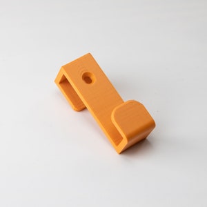 May include: Orange plastic hook with a rounded end. The hook has a small hole in the top for hanging.