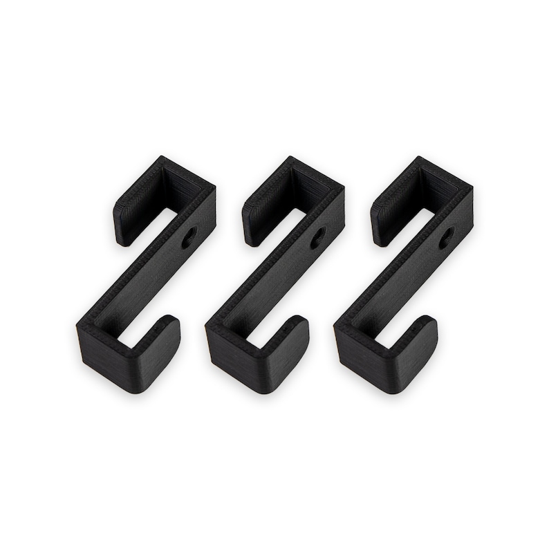 May include: Three black plastic hooks, each with a rounded top and a rectangular base. The hooks are arranged in a row, with the bases facing the viewer.