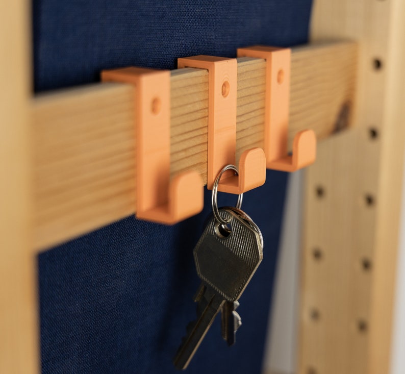 May include: Four orange plastic hooks mounted on a wooden wall rack with keys hanging from one of the hooks.