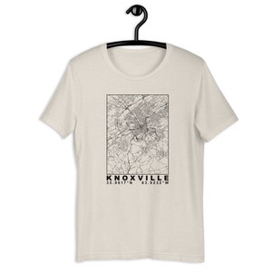 May include: A beige t-shirt with a black and white outline map of Knoxville, Tennessee. The text "KNOXVILLE" and the coordinates "35.9617°N 83.9232°W" are printed below the map.